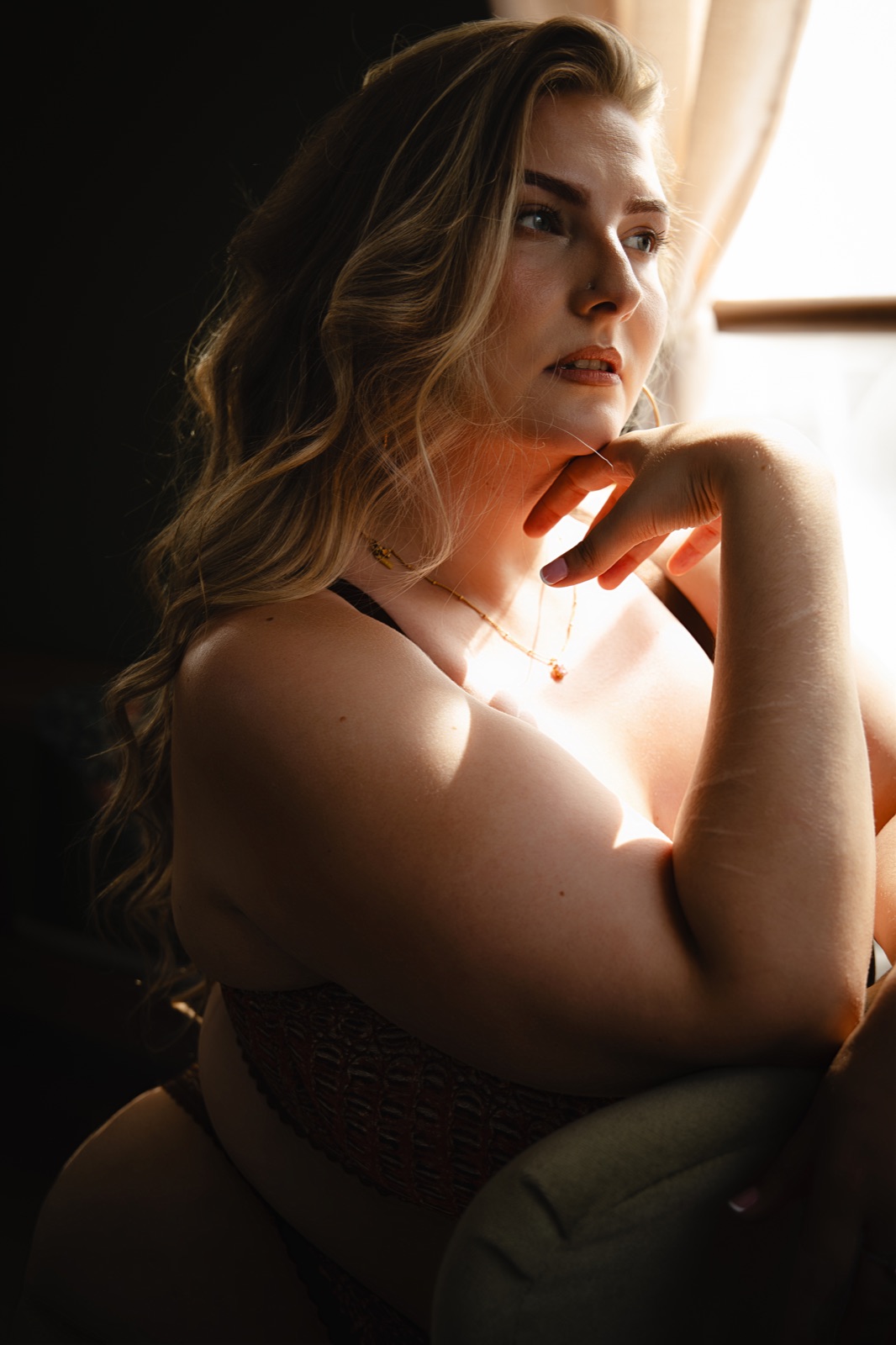 A woman resting her chin on her hand beside the sunlit studio window