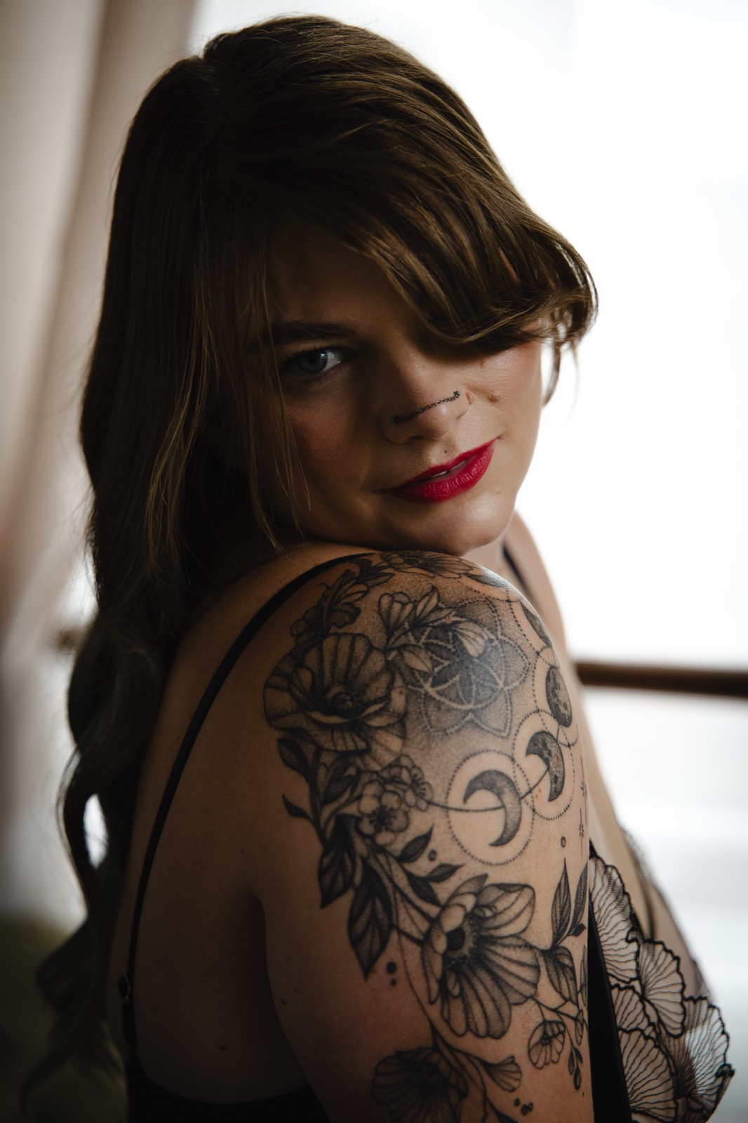 A woman looking over her tattooed shoulder towards the camera in soft window light