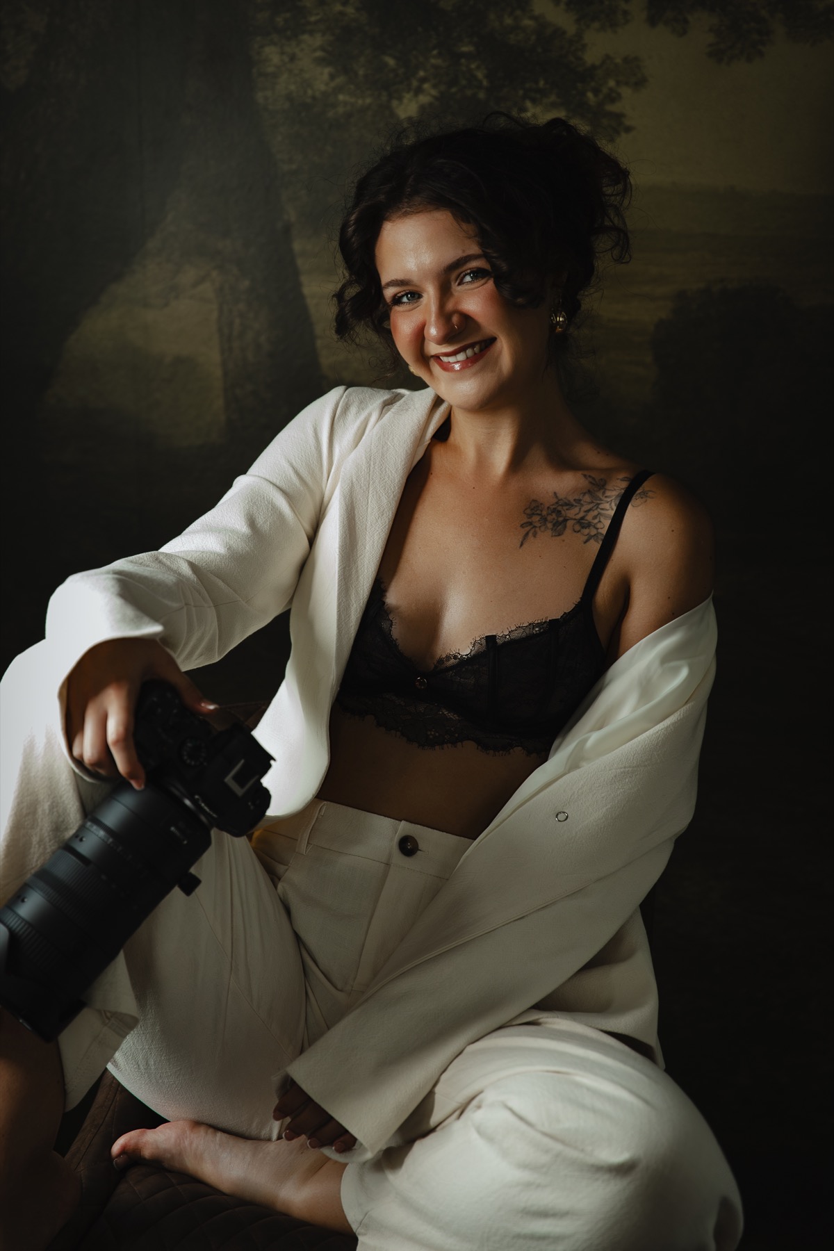 Jess smiling with her camera in the studio, wearing a white suit